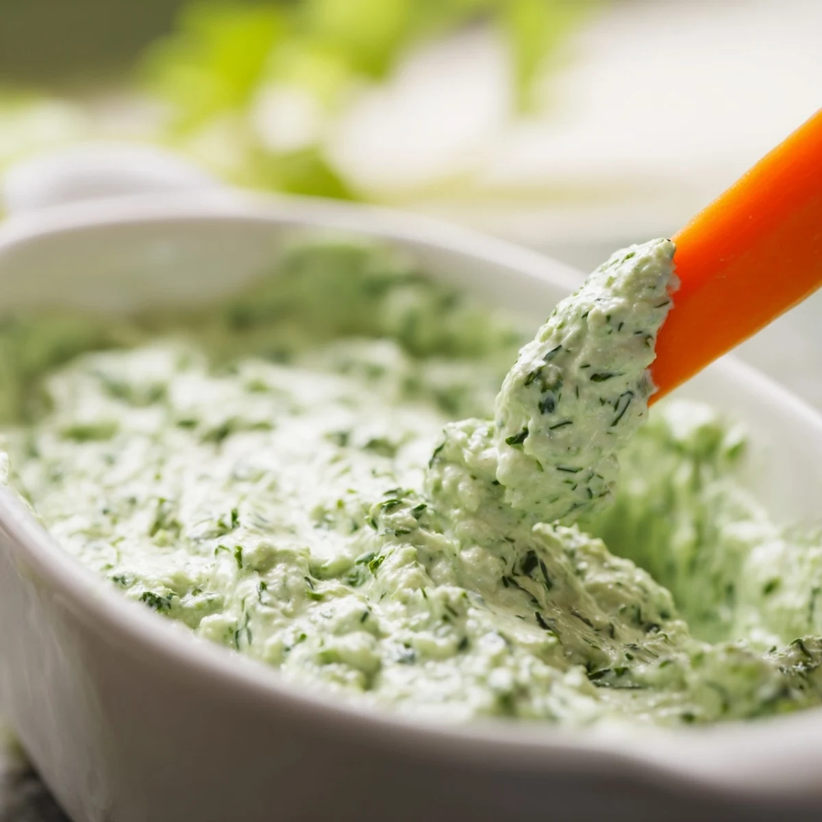 A chilled, vibrant green dip topped with fresh herbs, served alongside crispy carrot sticks and cucumber slices.