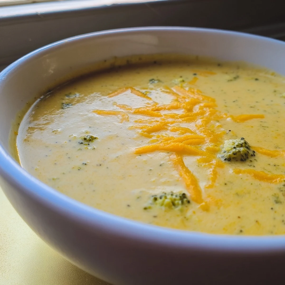 Freshly blended broccoli cheddar soup in a rustic mug, showcasing its velvety texture and vibrant green hue.  
