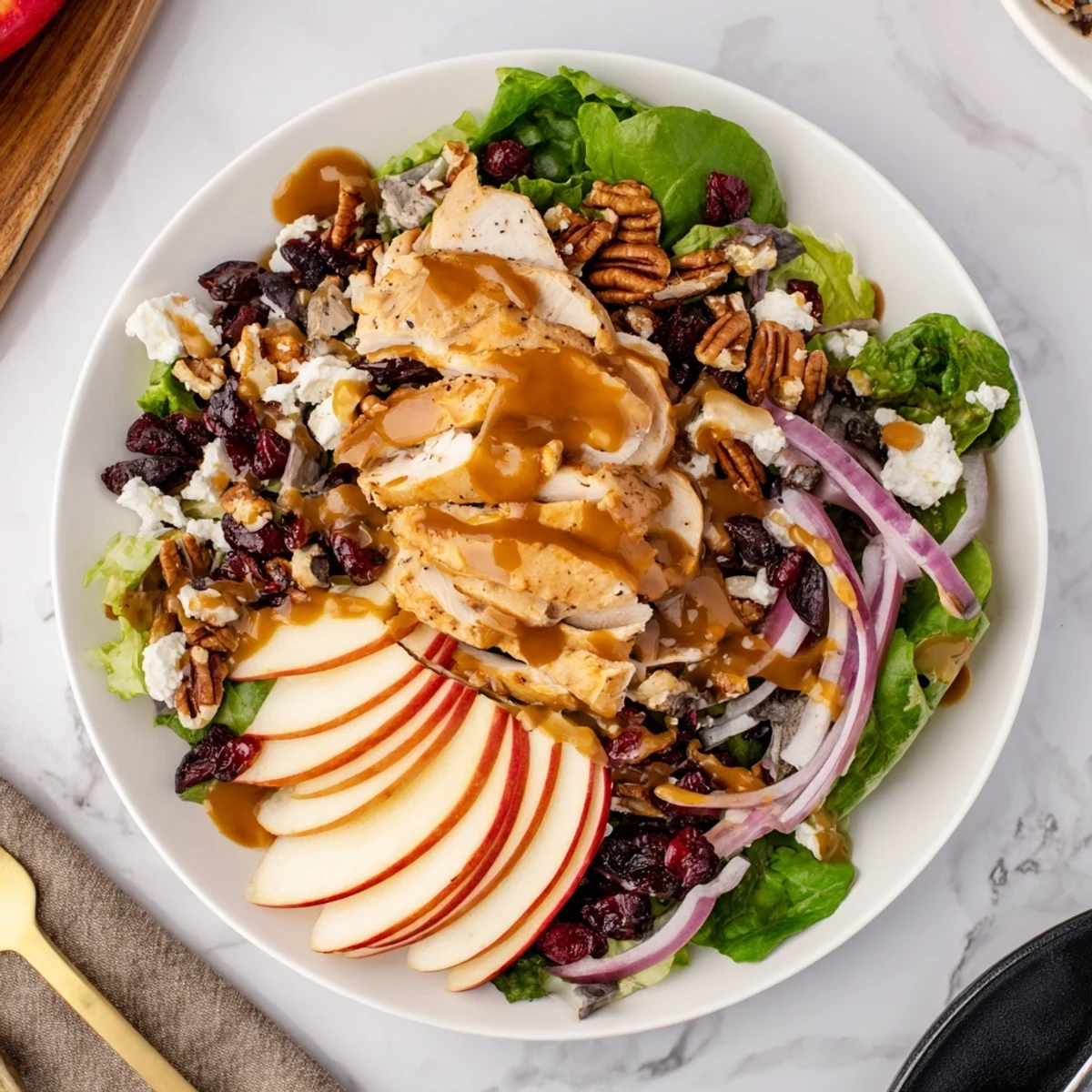 Freshly sliced apples and tender chicken layered over mixed greens on a white platter, ready for the caramel-pecan dressing.