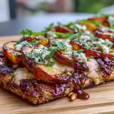 Grilled flatbread with sweet peaches, melted Brie, and smoky BBQ sauce, topped with fresh basil and arugula.  