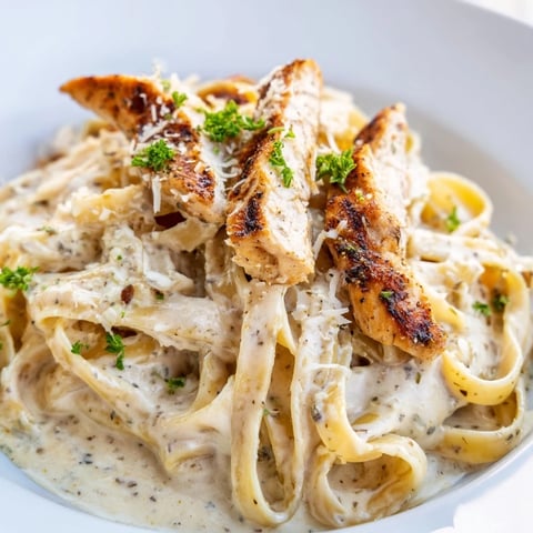 Golden-brown chicken strips nestle in a creamy skillet of fettuccine Alfredo, garnished with fresh parsley and a sprinkle of Parmesan cheese.  