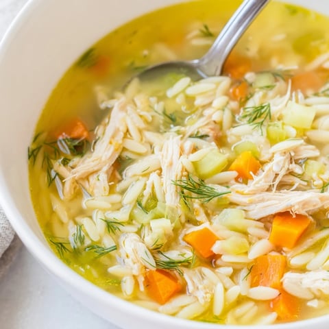 A steaming bowl of Chicken Lemon Orzo Soup with tender chicken, carrots, and fresh dill garnish.  