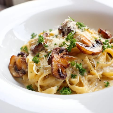 Freshly cooked fettuccine noodles are generously coated in a rich, creamy mushroom Alfredo sauce, garnished with chopped parsley.  