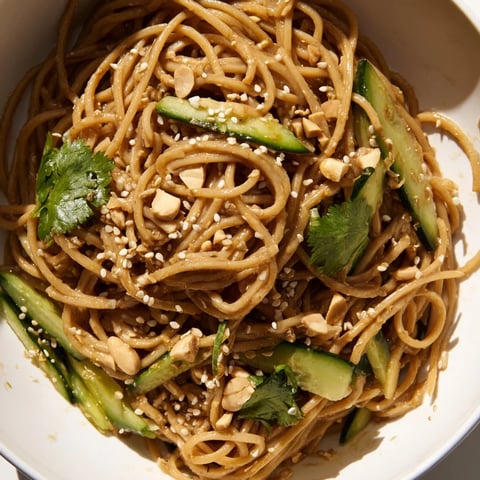 A close-up of Spicy Sesame Noodle Salad showing glossy noodles coated in chili oil, topped with fresh cucumber ribbons and toasted sesame seeds.