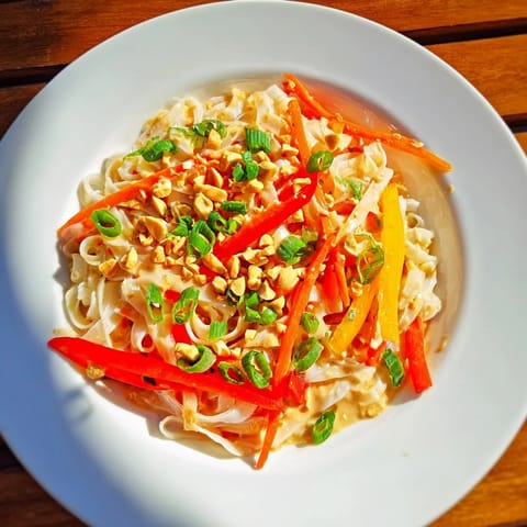 Close-up of freshly made spicy peanut noodles, garnished with peanuts and cilantro.