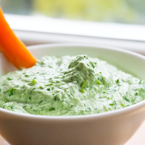 Creamy Green Goddess Salad Dip in a rustic bowl, surrounded by colorful tortilla chips and fresh vegetable crudités for dipping.