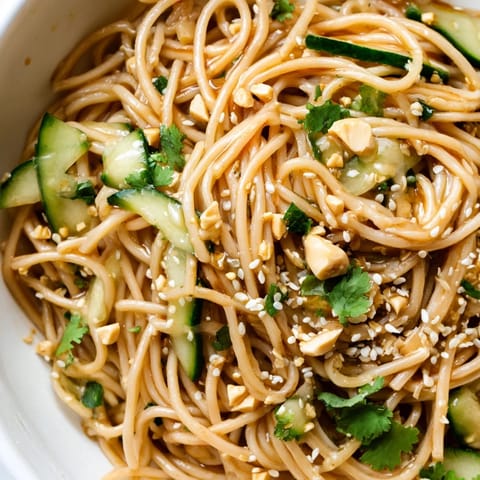 Freshly tossed Spicy Sesame Noodle Salad in a white bowl, garnished with chopped cilantro and crushed peanuts for a crunchy texture.