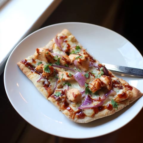 A close-up of BBQ Chicken Flatbread with tangy sauce, sliced chicken, and fresh cilantro garnish.
