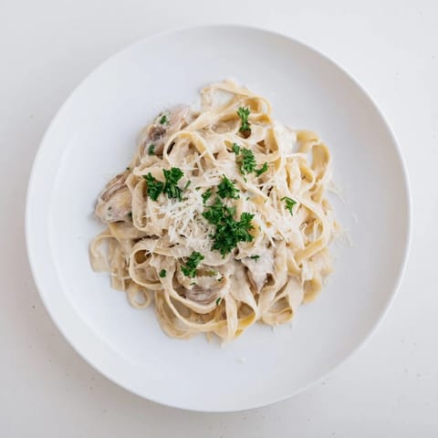 A close-up of roasted garlic cream pasta twirling on a fork, highlighting the silky texture and rich, golden sauce.