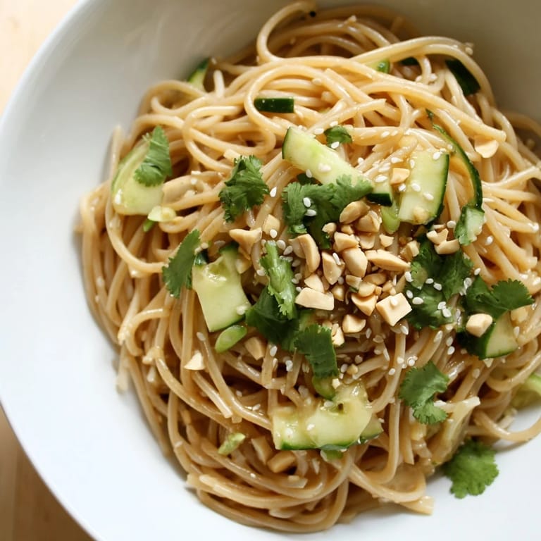 Overhead view of Spicy Sesame Noodle Salad on a rustic table, featuring vibrant green herbs and a drizzle of sesame-chili dressing.