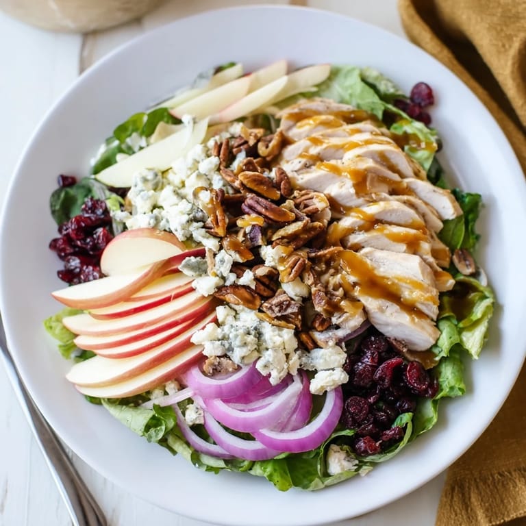 A close-up of a serving of Caramel Apple Chicken Salad showing feta, cranberries, and thinly sliced red onion.